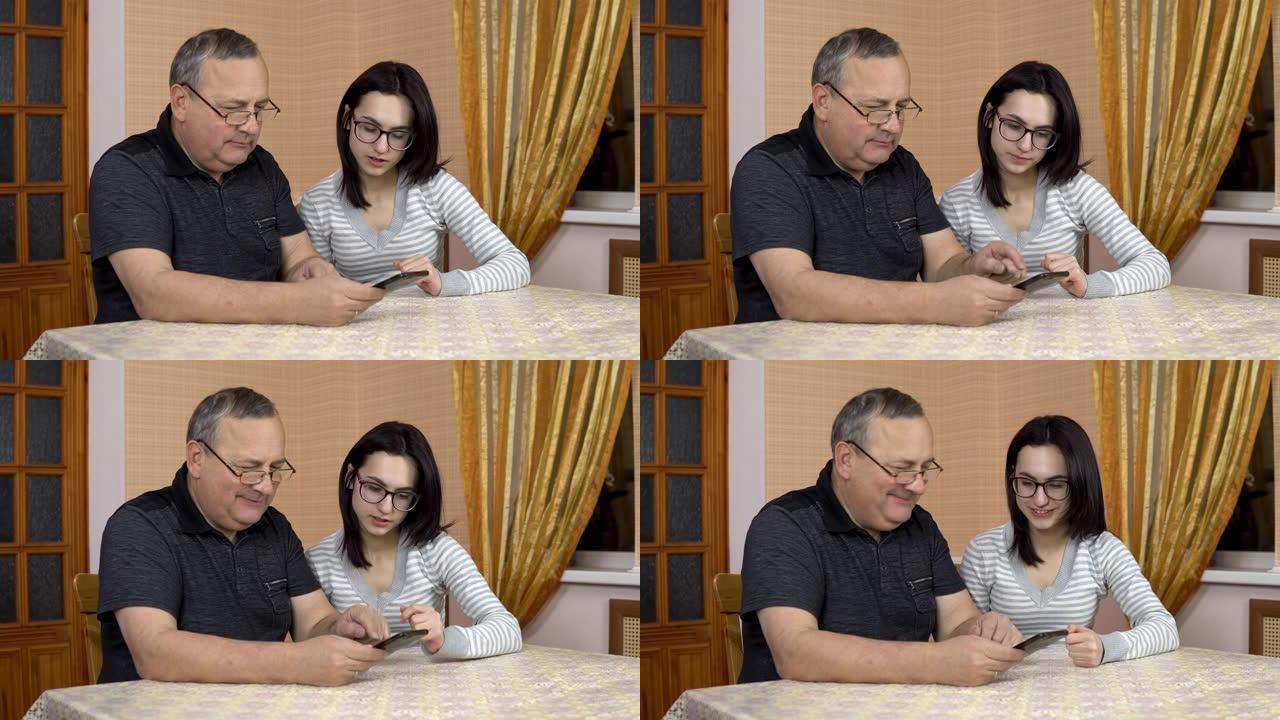 女儿教父亲如何使用电话。一位年轻女子向她的老父亲展示了在哪里推电话。一家人坐在舒适的房间里。