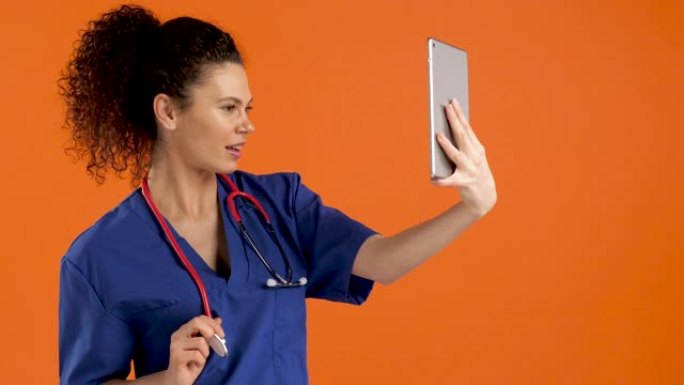 年轻女医生在橙色背景下用数字平板电脑自拍，慢动作