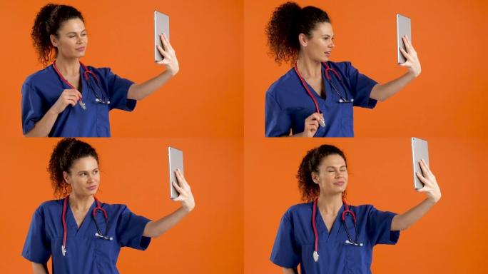 年轻女医生在橙色背景下用数字平板电脑自拍，慢动作