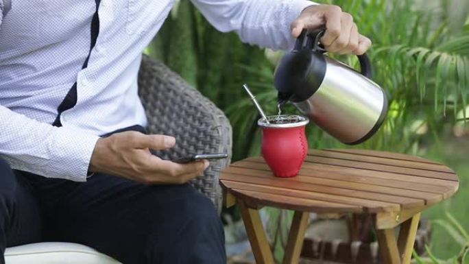 使用智能手机放松和在咖啡馆独自坐在餐桌旁喝yerba mate茶的男人的手的特写镜头。人，现代技术和