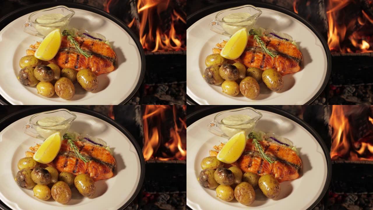 烤鱼放在白盘上，配土豆，柠檬和酱汁，明火，红煤，烟，柴火