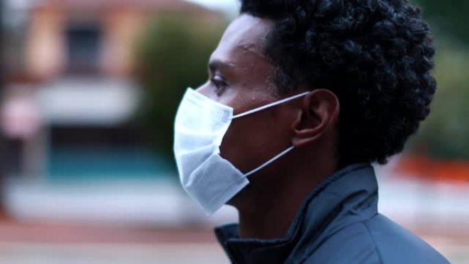 黑人男子戴着外科医疗口罩在外面的城市向前走