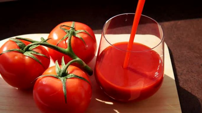 美味的番茄汁与成熟的红色西红柿玻璃杯。将番茄汁倒入玻璃杯中