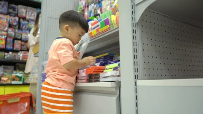 亚洲蹒跚学步的男孩在文具店挑选铅笔。