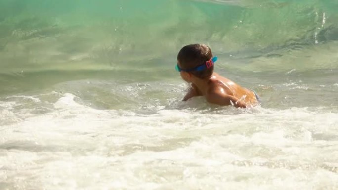 海浪的海浪覆盖了一个穿着泳衣和游泳镜的小男孩