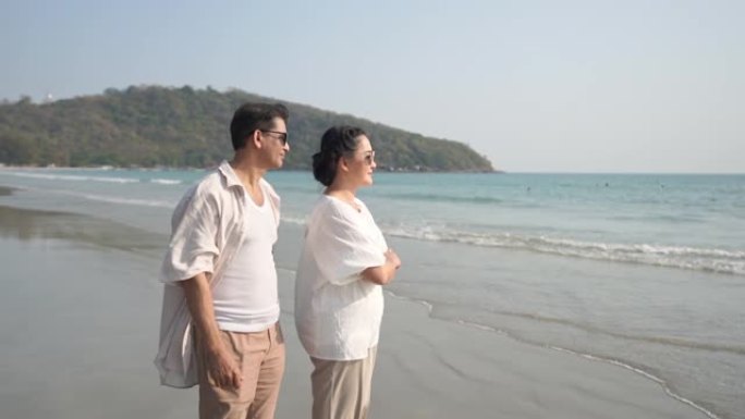 快乐的亚洲高级丈夫在海滩上拥抱妻子，微笑着望着大海的高清慢动作。退休老年夫妇男女家庭在浪漫结婚周年纪