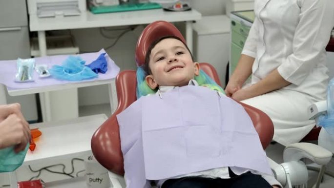 微笑的男孩坐在牙科椅上。医生和他的助手正准备接收。男孩在看相机。儿童牙科。儿童医生。你需要保护你的牙