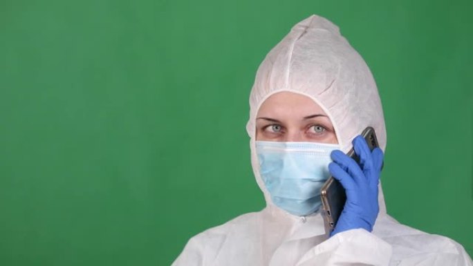 年轻的女军医穿着白色雾蒙蒙的外套在电话上讲话，戴着防护口罩，绿色背景上戴着橡胶手套
