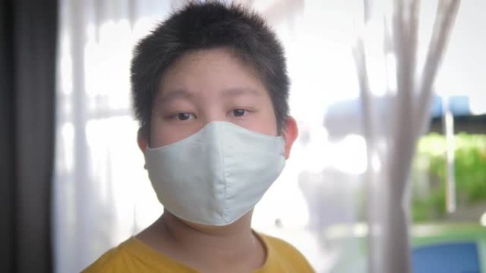亚洲生病的年轻青春期男孩戴着口罩站在家里的窗户附近，检疫概念。