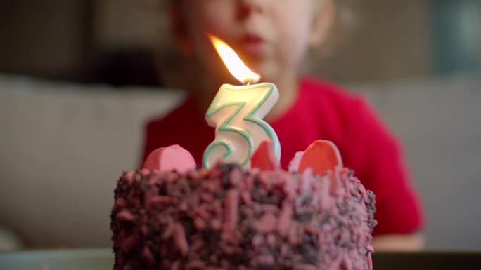 孩子用慢动作吹出巧克力生日蛋糕上的3号蜡烛的特写镜头。三岁的女孩庆祝生日。