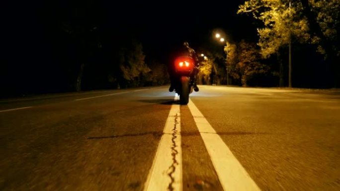 戴着头盔和皮夹克的骑自行车的人在夜间高速公路上坐在摩托车上，开始骑行。男人在晚上开始骑摩托车。自由和