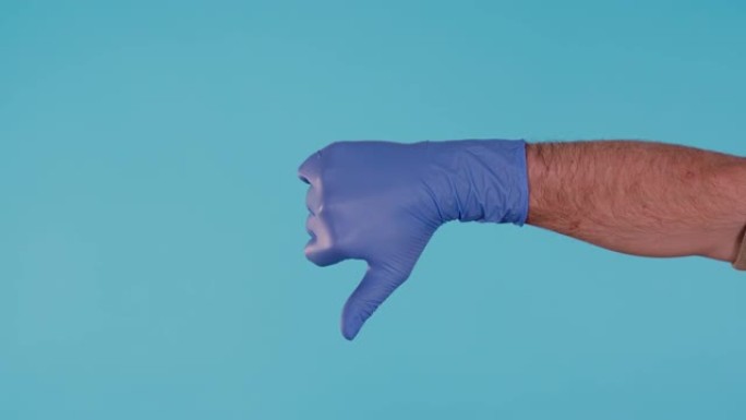 蓝色手术乳胶手套的男性手显示拇指向下孤立在蓝色背景