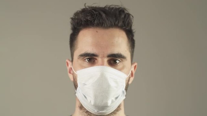 在法国新型冠状病毒肺炎大流行病毒期间，戴着外科口罩、棕色头发和眼睛的孤立男子面对工作室的镜头。4K 