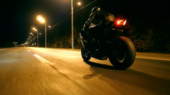 男子在夜间城市街快速骑现代运动摩托车。摩托车手在空旷的道路上骑摩托车。黄昏时开车的人。自由和冒险的概