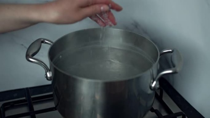 一个女人的特写镜头，在煤气炉上的平底锅中向沸水中加盐