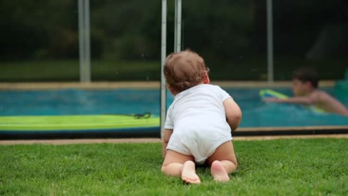婴儿在后院的草地上爬行，观察儿童在游泳池里玩耍。婴儿爬到外面