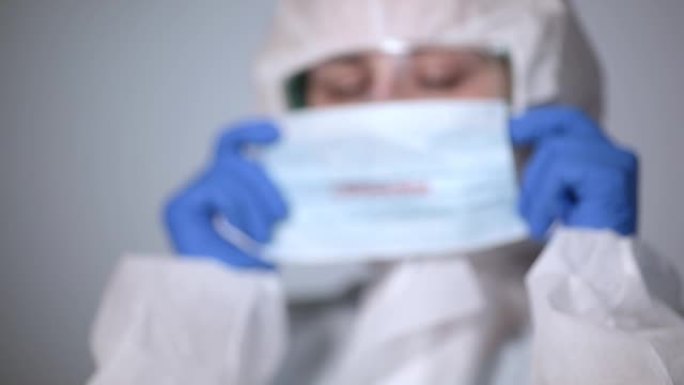 年轻的女孩医生在她的脸上戴上面具，上面冠状病毒一件白色的保护性雾状外套的铭文