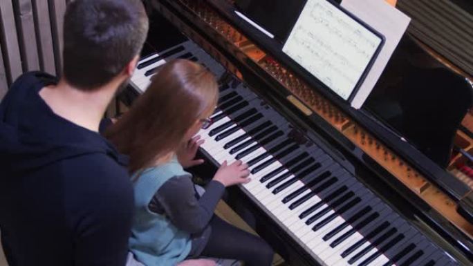 爸爸给女儿教钢琴。小女孩在家学钢琴。俯视图。在家的钢琴课。从父亲那里学习钢琴的孩子