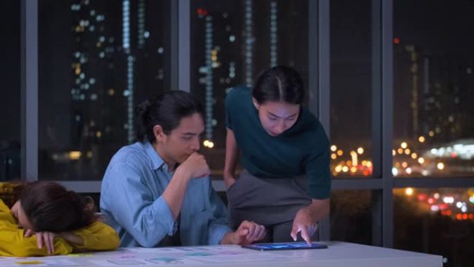 亚洲ux/ui设计师讨论夜间现代办公室桌上的移动应用界面线框设计。工作后期创意数字开发机构