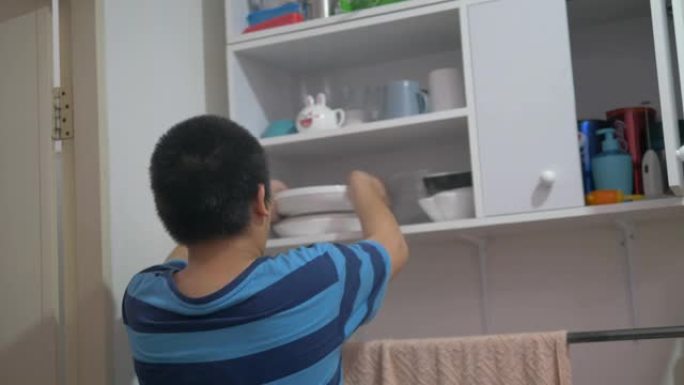 亚洲青春期男孩拿着白色盘子，放在架子橱柜上。
