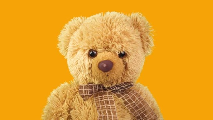 橙色背景上的泰迪熊。运动中的儿童玩具。最喜欢的玩具