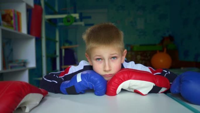 一个心烦意乱的孩子在检疫时看着窗外。戴拳击手套的悲伤男孩坐在桌子旁。