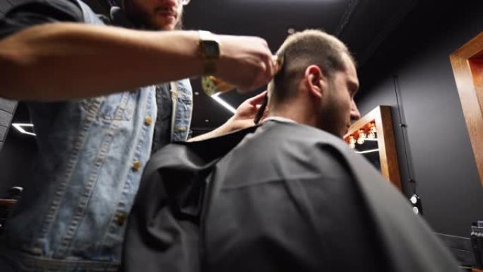时髦的理发师在理发店用理发剪胡子的男人的头发。沙龙中的男士发型和理发。用修剪器梳理头发。理发师在复古