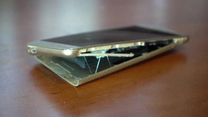 膨胀的智能手机电池。电池故障的智能手机损坏。木制背景上损坏的手机。