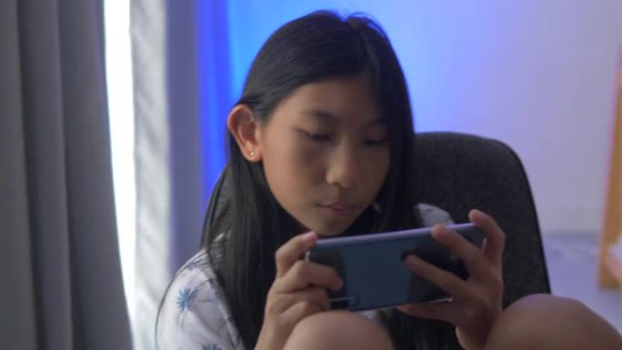 亚洲女孩在窗户附近玩网络游戏，带发光二极管灯背景。