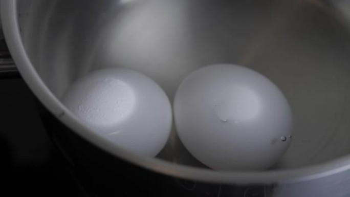 两个生白鸡蛋在不锈钢锅中煮沸，放在沸水中。健康的天然蛋白质早餐烹饪。鸡蛋煮沸了。热水鸡蛋。电影4k视