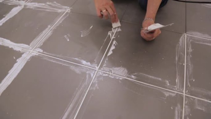 工人在地板上瓷砖之间的抹布接缝