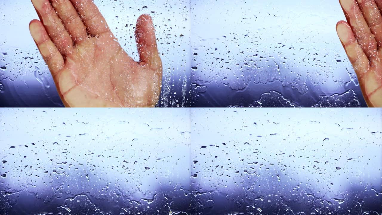 雨后手握在潮湿的窗户上。背景模糊。特写