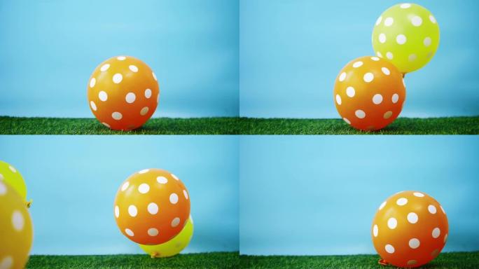 黄色和橙色的气球落在绿色的草地上，慢动作。