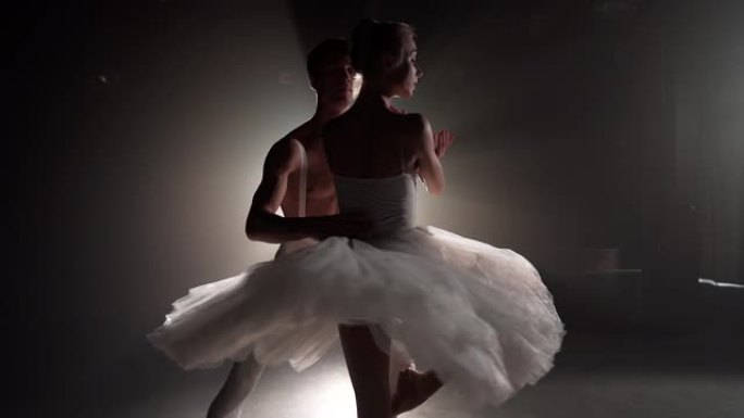 专业芭蕾舞情侣在大舞台上的聚光灯下跳舞。泛光灯背景上美丽的年轻女人和男人。情感二重唱表演舞蹈艺术。慢