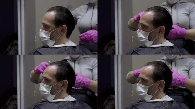 戴着防护口罩的客户耐心地坐着，而理发师则由发型师梳理头发，并准备剪掉头发。男子在大流行检疫期间参观美