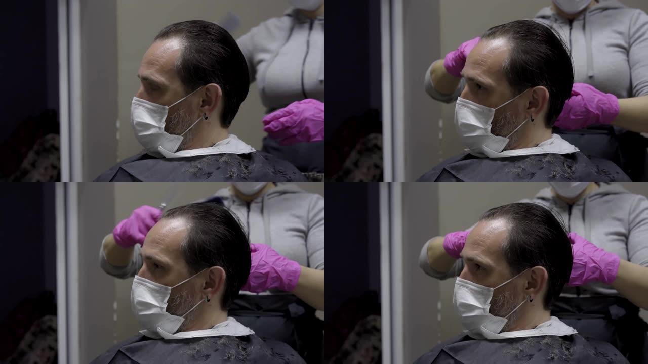 戴着防护口罩的客户耐心地坐着，而理发师则由发型师梳理头发，并准备剪掉头发。男子在大流行检疫期间参观美