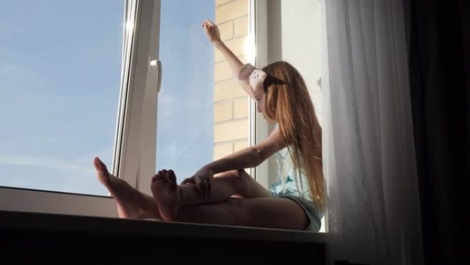 十几岁的女孩坐在窗台上，看着窗外。年轻女孩花时间在家里隔离从新型冠状病毒肺炎。检疫流行。呆在家里的概