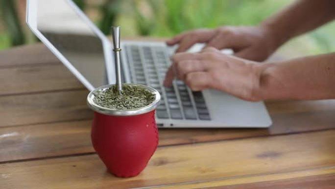 在家庭办公室工作在笔记本电脑上喝yerba伴侣茶的女人。慢动作。健康的生活方式理念。