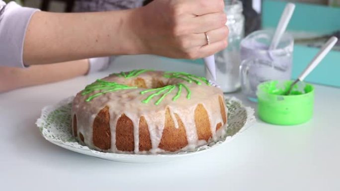 用绿色元素装饰的糖纸杯蛋糕。女人用糕点袋添加物品。