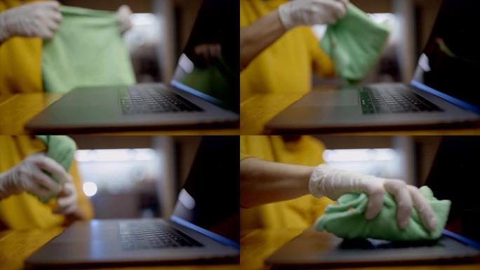 戴着手套的年轻人用抹布清洁笔记本电脑键盘