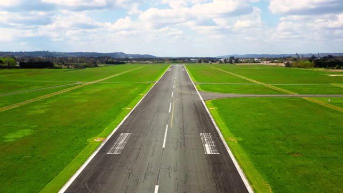 无人机在天空中越来越高的着陆跑道上的鸟瞰图。空空的飞机跑道周围有绿草，天空多云-4K