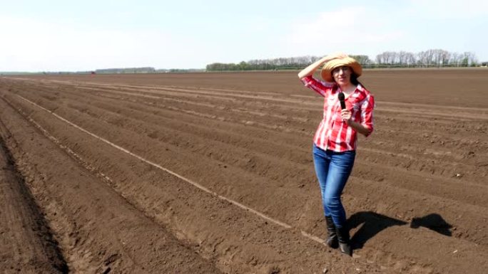 女记者为电视新闻报道讲述现代农业种植。耕田背景。播种时间或收获时间。温暖的晴天