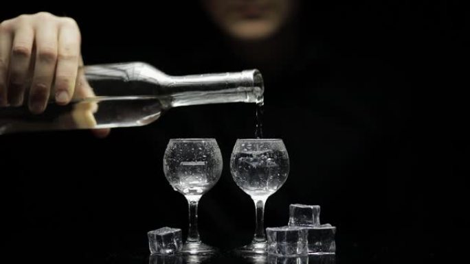 酒保把冷冻伏特加从瓶子里倒入两杯加冰的杯子里。黑色背景