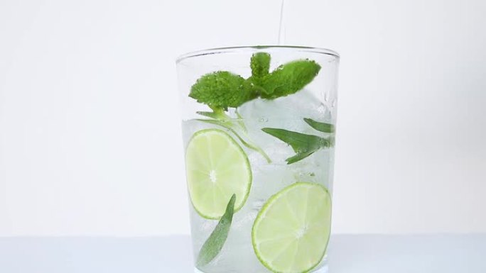 喝清爽的夏季鸡尾酒柠檬水配冰、龙蒿、酸橙、薄荷，倒入玻璃杯特写