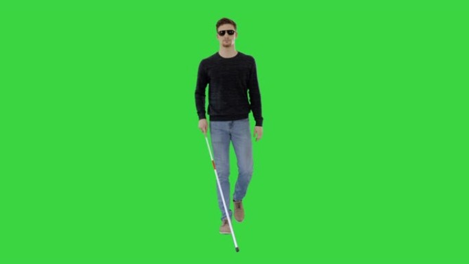 盲人年轻人用棍子在绿色屏幕上行走，色键