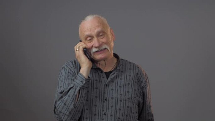 穿着深色衬衫的退休男子手持黑色智能手机并讲话