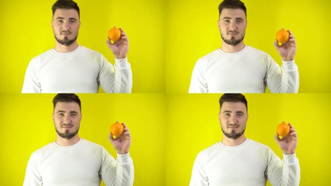 一个年轻人手里拿着一个新鲜的橘子。一个穿着白色运动衫的男人眨眨眼，微笑着。适当营养的概念。黄色简单背