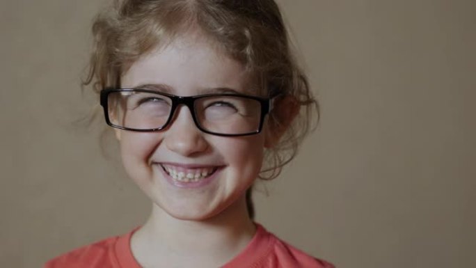 戴眼镜的肖像小女孩看着相机。年轻的孩子戴着眼镜看着相机开心地笑。特写。好奇的小女孩肖像。面对有趣沉思
