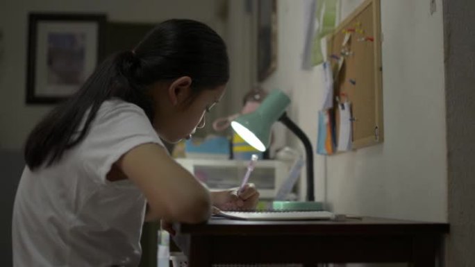 亚洲女少年晚上在办公桌上做作业时学习和写作。