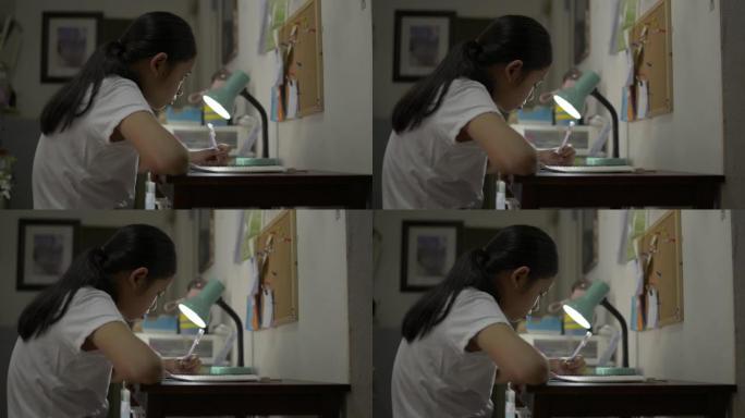 亚洲女少年晚上在办公桌上做作业时学习和写作。